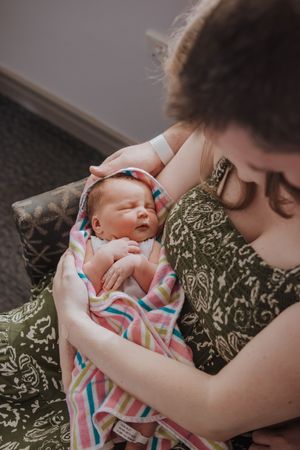 A tender moment shows a newborn baby being cradled and kissed in a nurturing embrace against a green background.