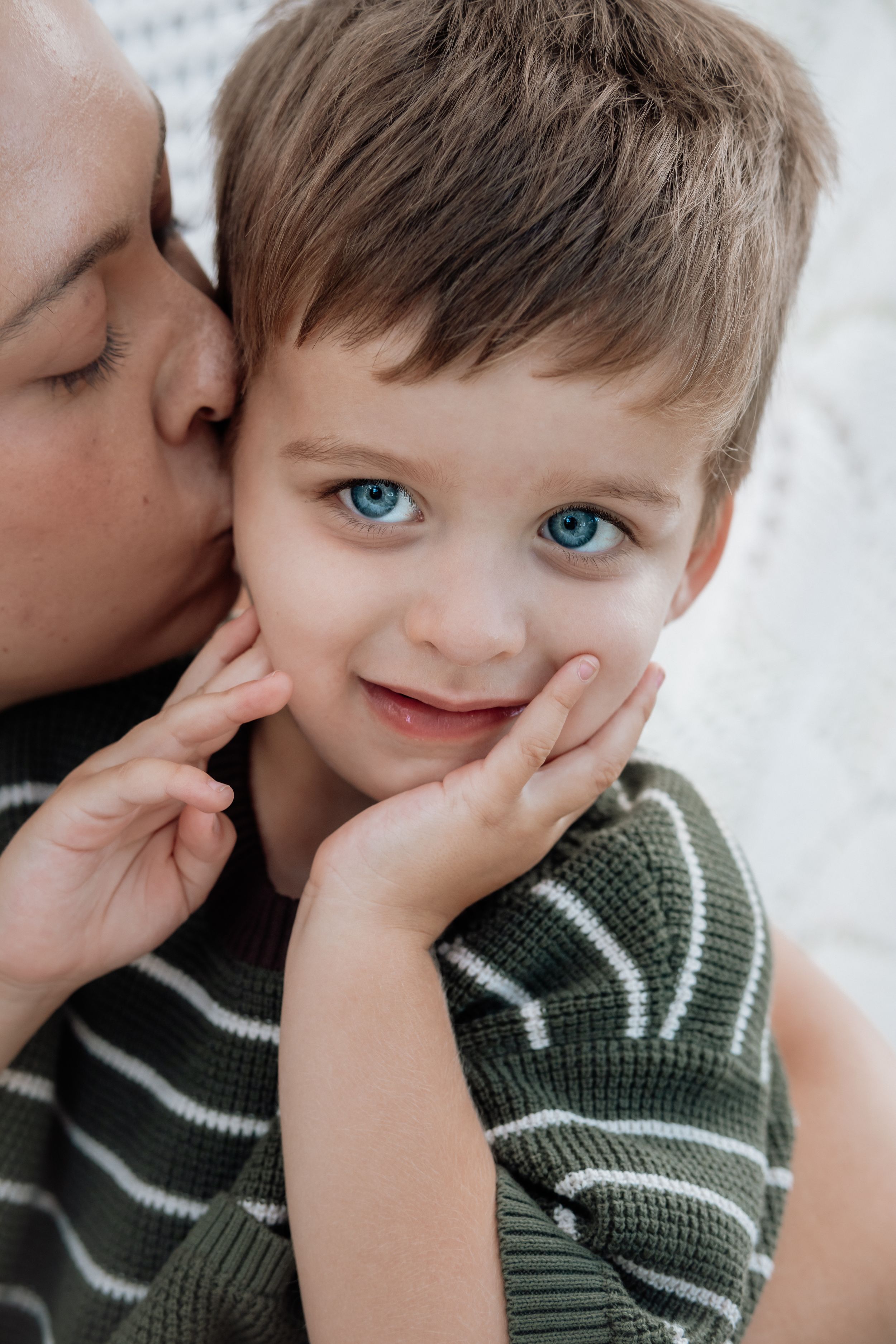 A series of four connected photos showing a child in a green striped sweater being kissed on the cheek.
