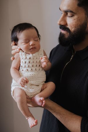 A series of tender moments showing a baby in a white crocheted romper being held against a dark sweater.