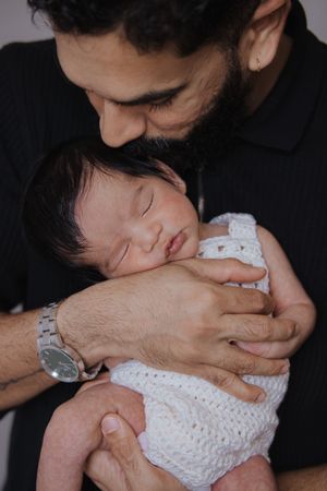A tender moment between parent and sleeping baby wearing a white knitted outfit.