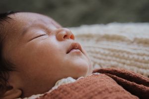 Close-up of sleeping baby in brown knit blanket with peaceful expression.