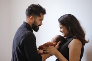 Parents lovingly gazing at their newborn baby against white wall background.