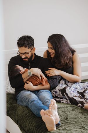 A family shares an intimate moment while bottle feeding their newborn on a green blanket.
