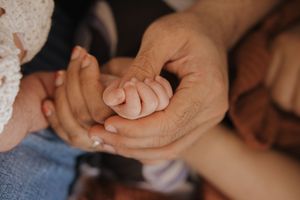Close-up of gentle hands cradling a tiny baby's fingers in soft natural light.
