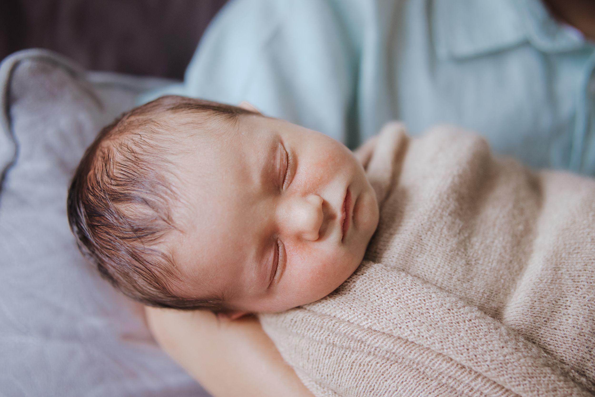Sleeping baby wrapped in beige blanket lying on soft white bedding in peaceful slumber.