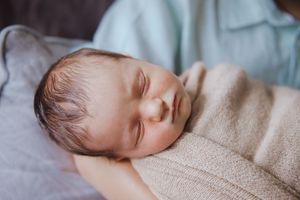 Sleeping baby wrapped in beige blanket lying on soft white bedding in peaceful slumber.