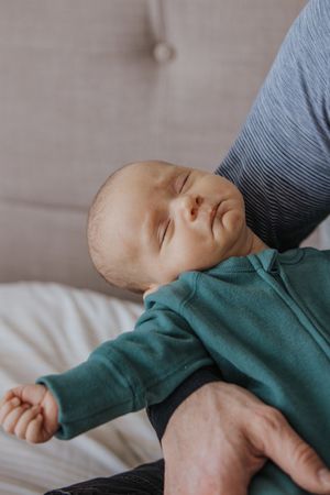 A sleeping baby wearing a green sweater lies peacefully on white bedding in a series of connected photos.