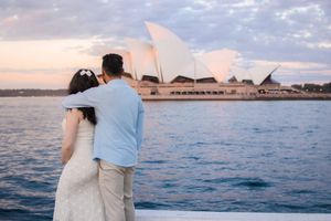 Couple admires Sydney Opera House from harbor viewpoint during golden hour.