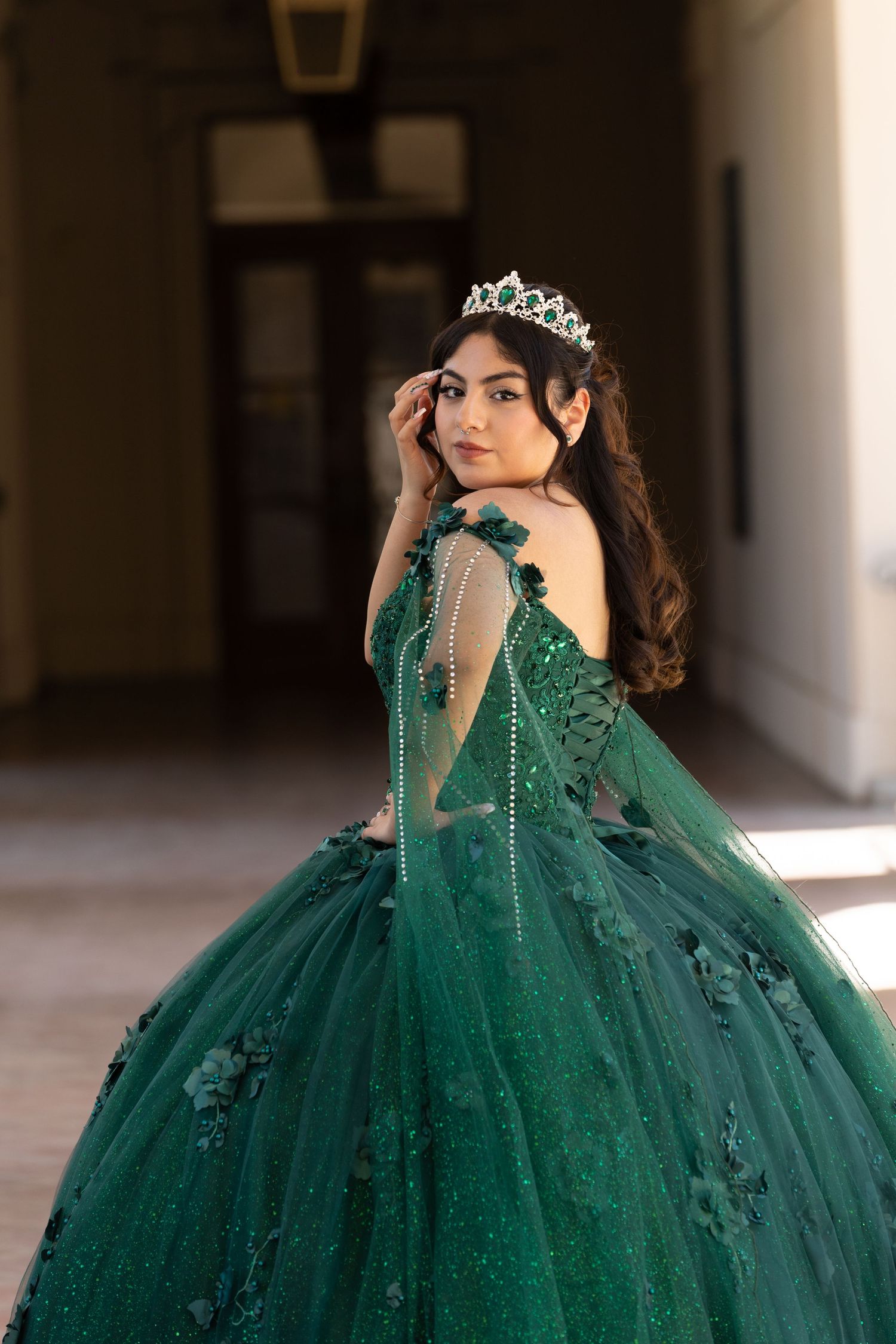 Elegant emerald green ball gown with floral appliques and crystal details sparkles in dramatic indoor lighting.