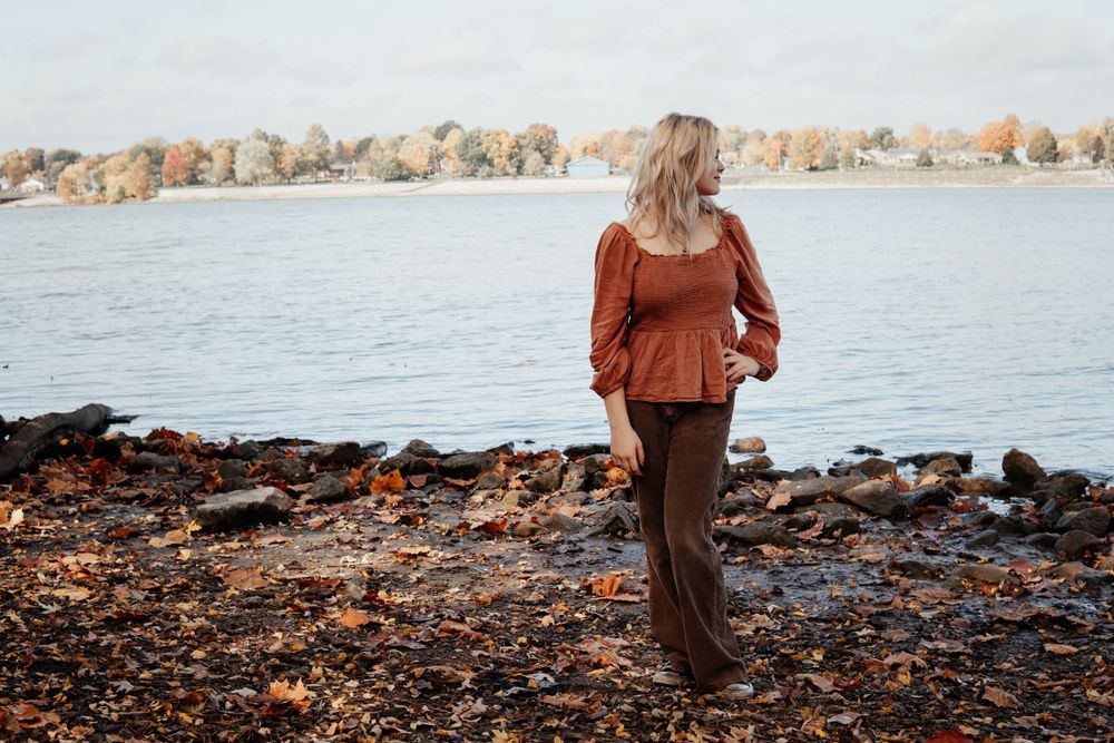 A peaceful scene of someone walking along a rocky shoreline beside a calm lake at sunset.