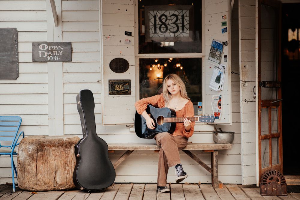 A musician sits on a porch with a guitar case nearby at house number 1831.