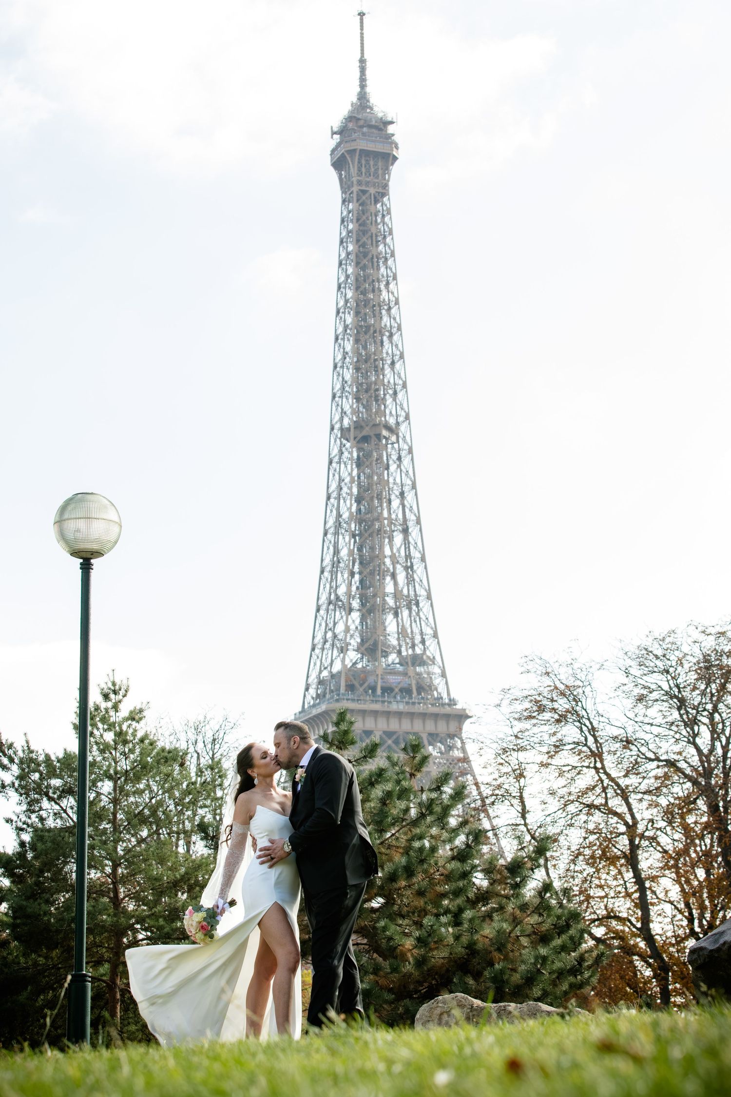 Rare, secret view of the Eiffel Tower: A couple kisses in a hidden garden with lush trees. Epic Paris photography by Julien LB Photography