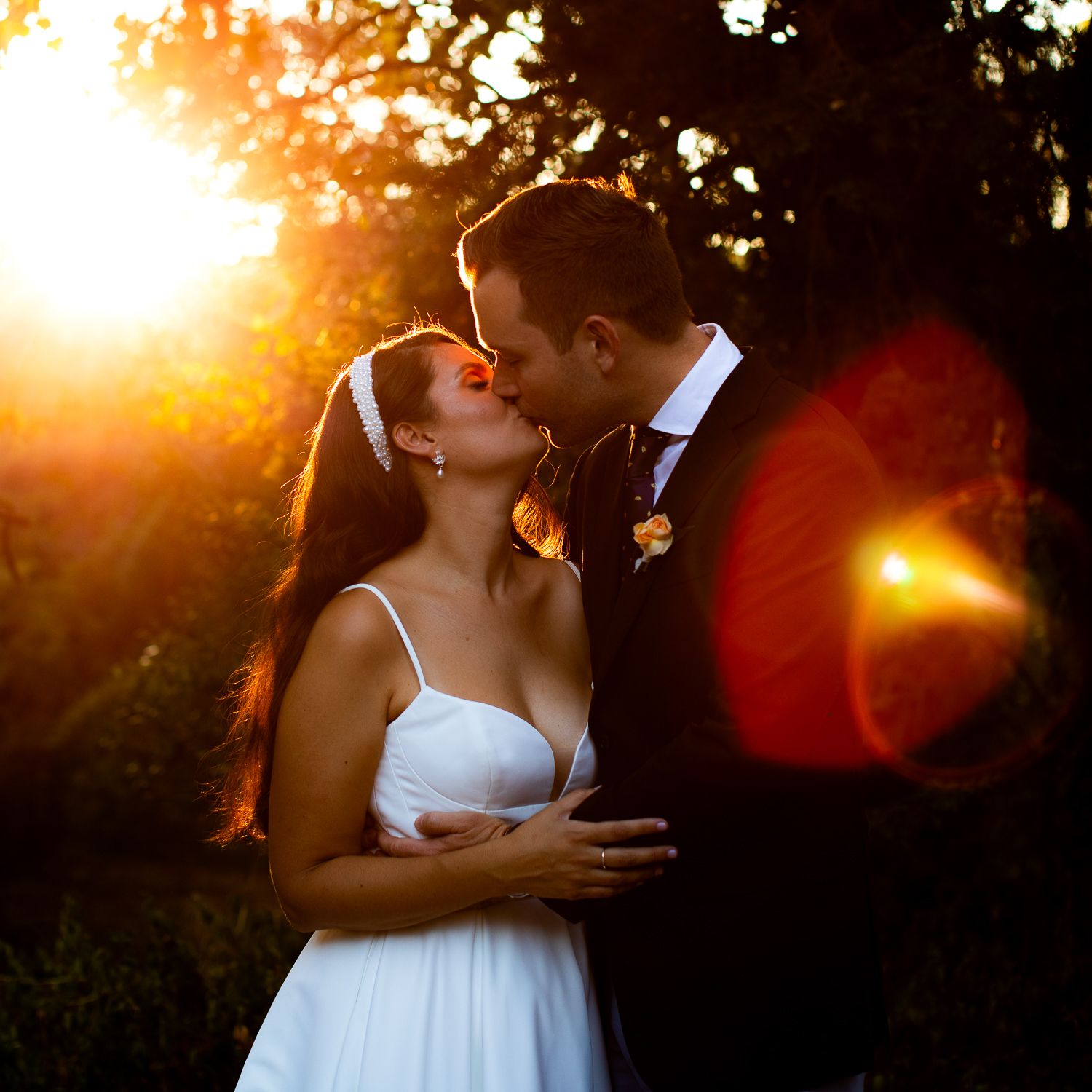 A romantic sunset wedding moment captured with golden light and lens flare in an outdoor garden setting.