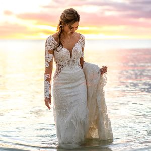 Long sleeve lace wedding dress with plunging neckline captured at sunset near ocean waters.