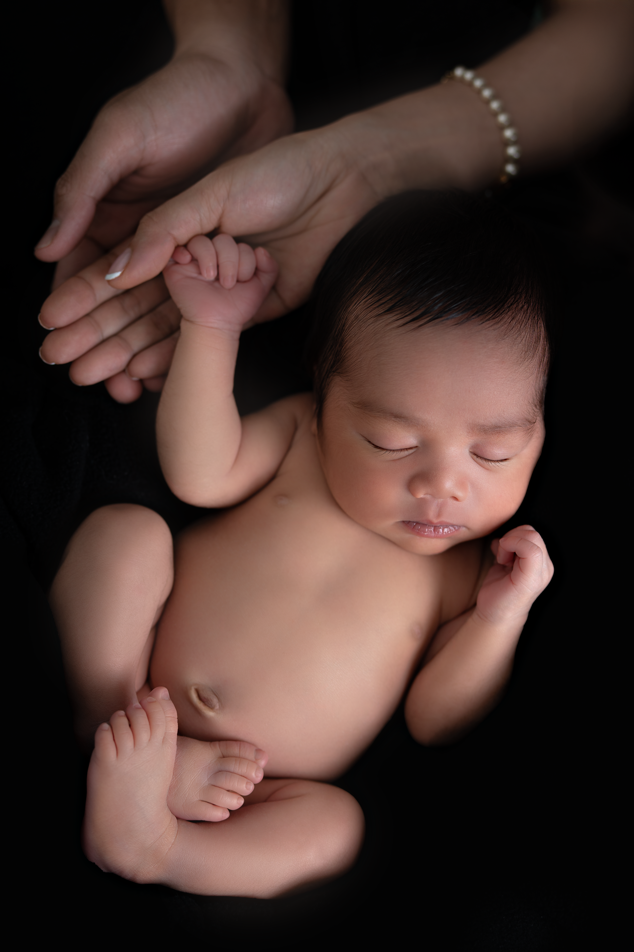 Sleeping newborn baby held gently by mother's hands on black background, peaceful infant portrait photography.