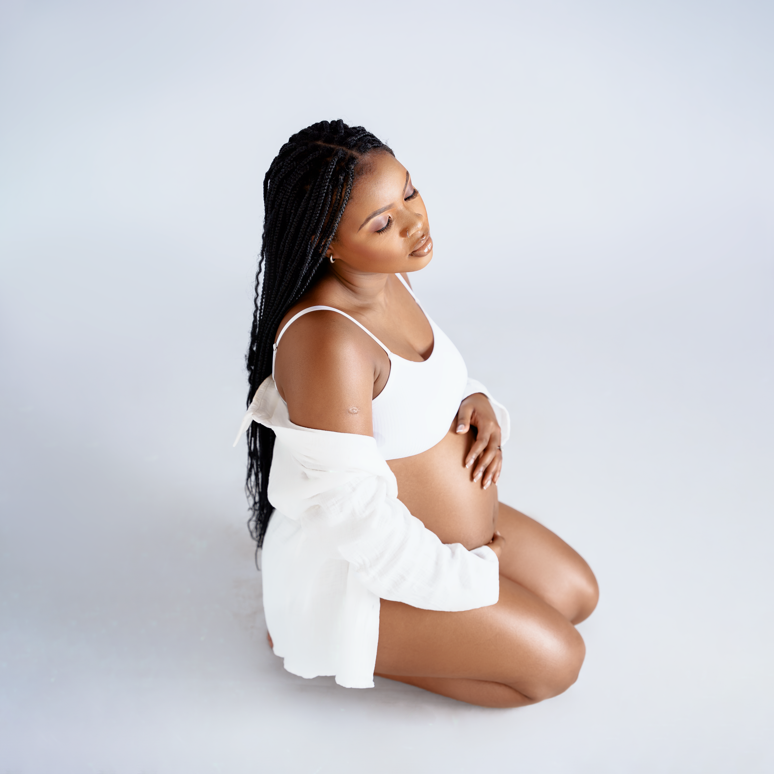 Expectant mother in white clothing poses serenely during maternity photoshoot.