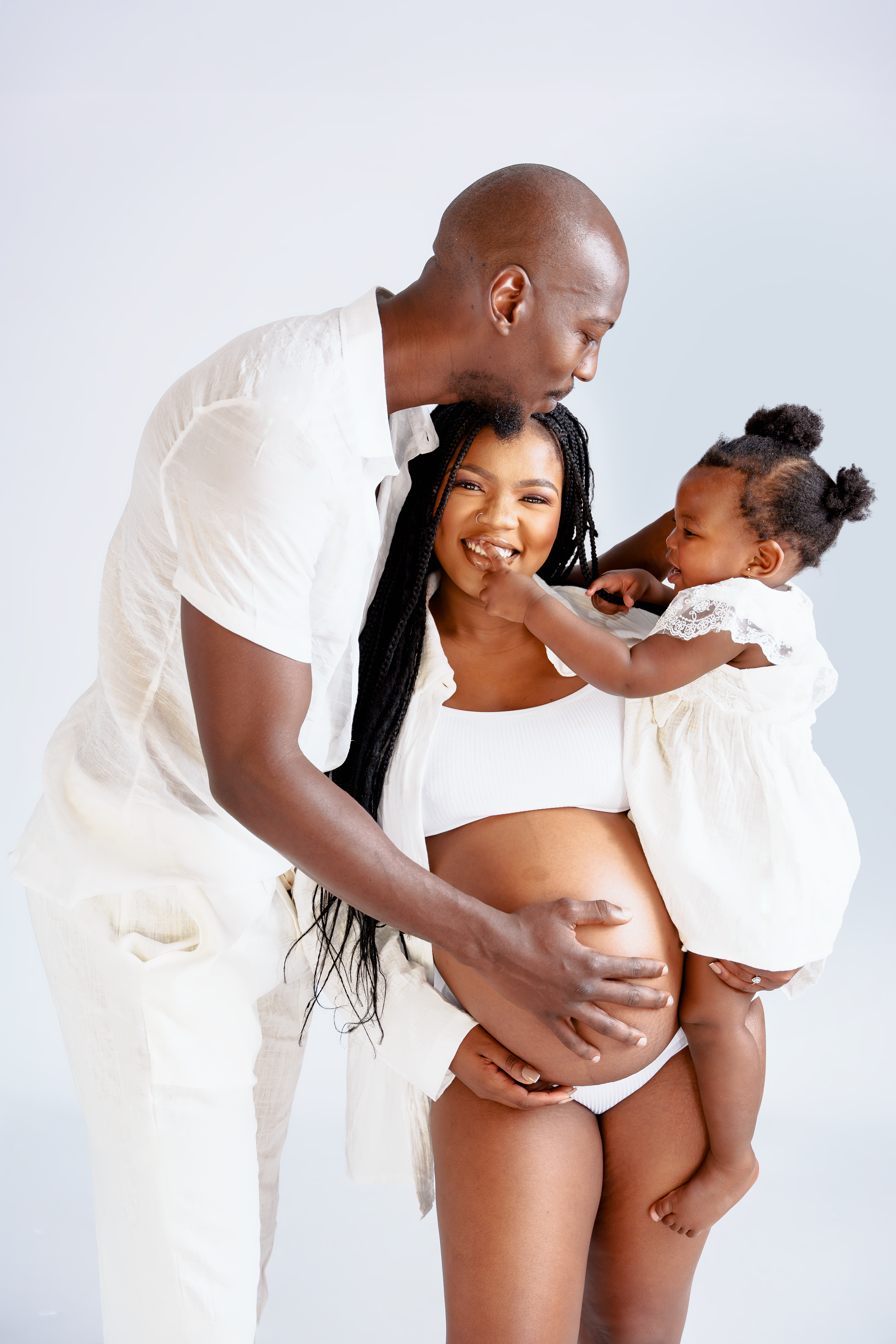 Family portrait with pregnant woman in white, child in white dress, and parent in matching attire.