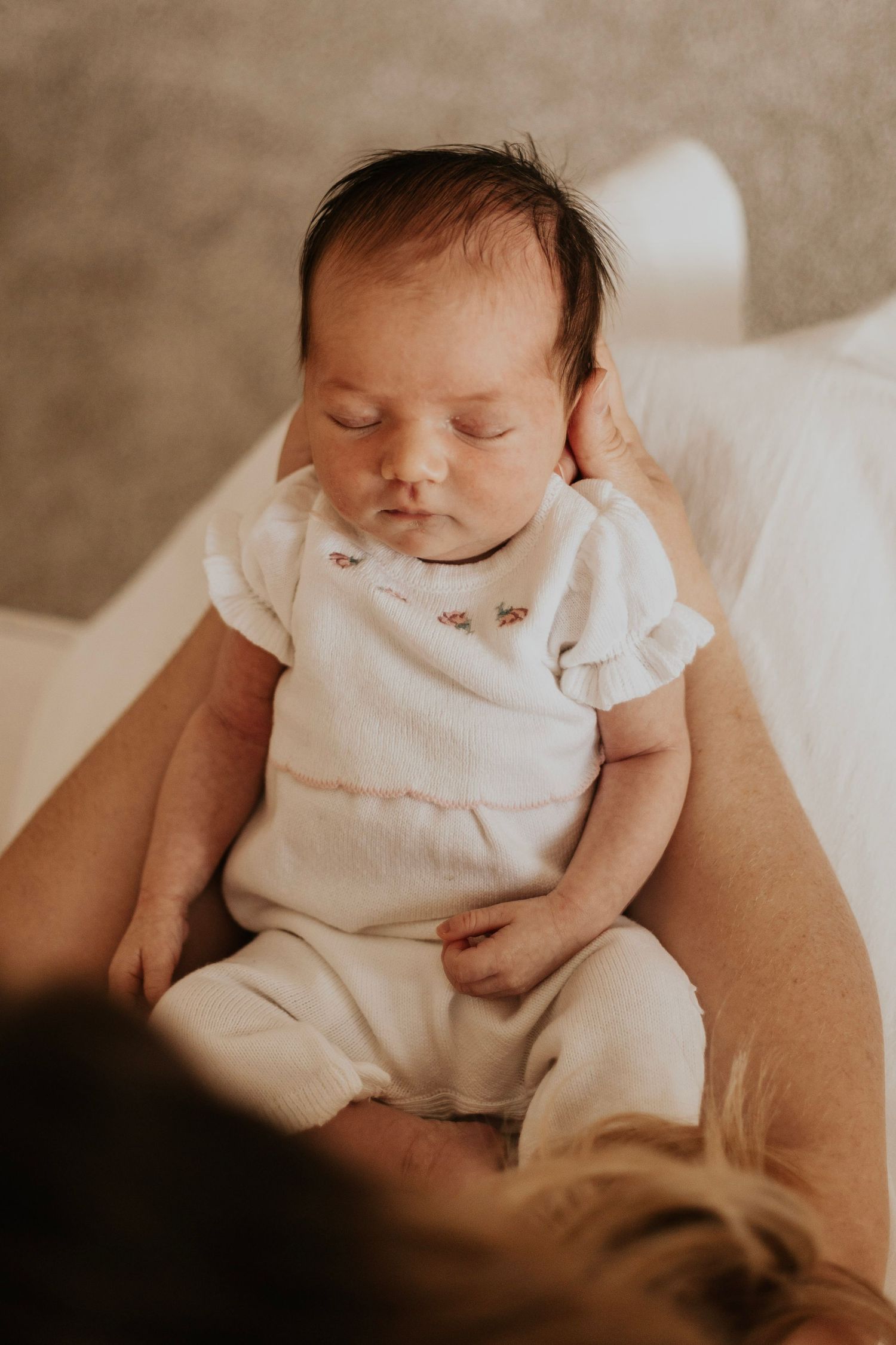 A sleeping newborn baby wearing a white onesie rests peacefully.