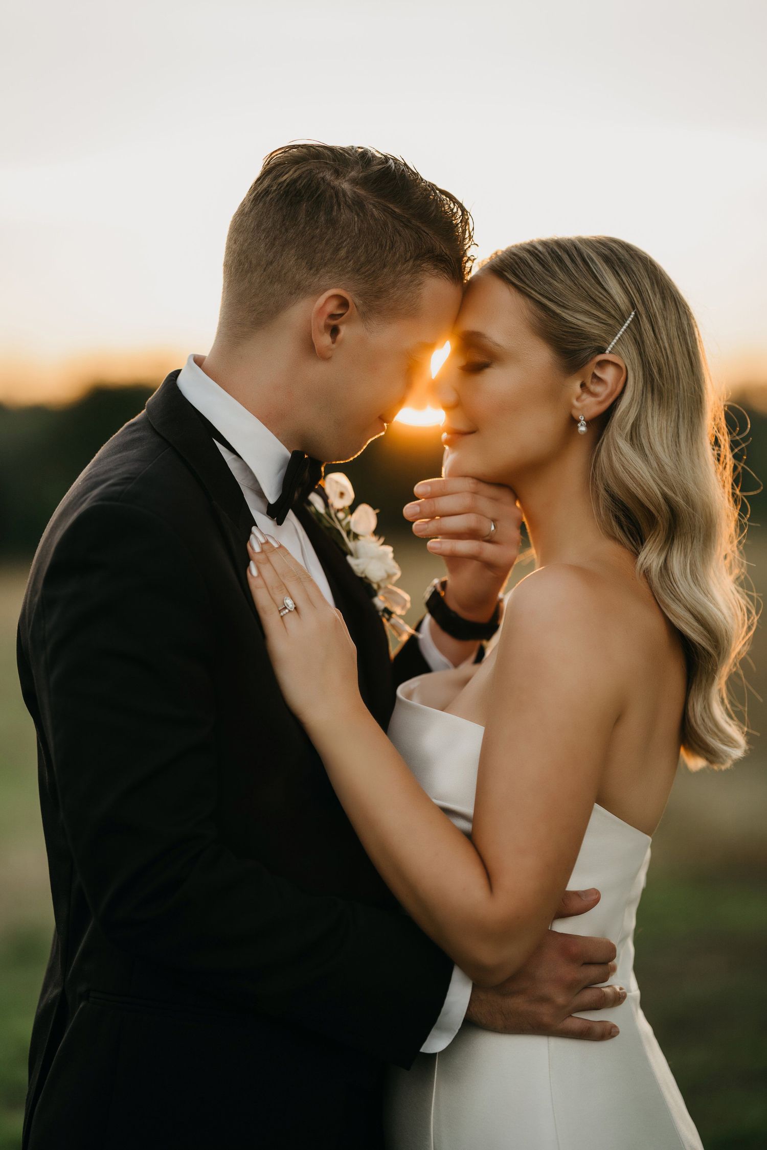 Romantic sunset wedding photo with couple embracing outdoors, golden light illuminating their intimate moment.