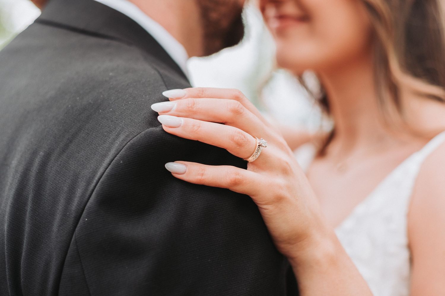 A close-up shot of a couple's embrace at their wedding, showing the bride's delicate hands and sparkling engagement ring.
