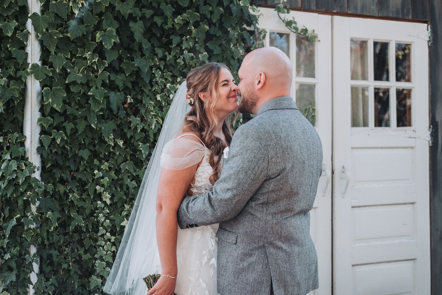 A tender moment between a couple against a white door with ivy growing around it.