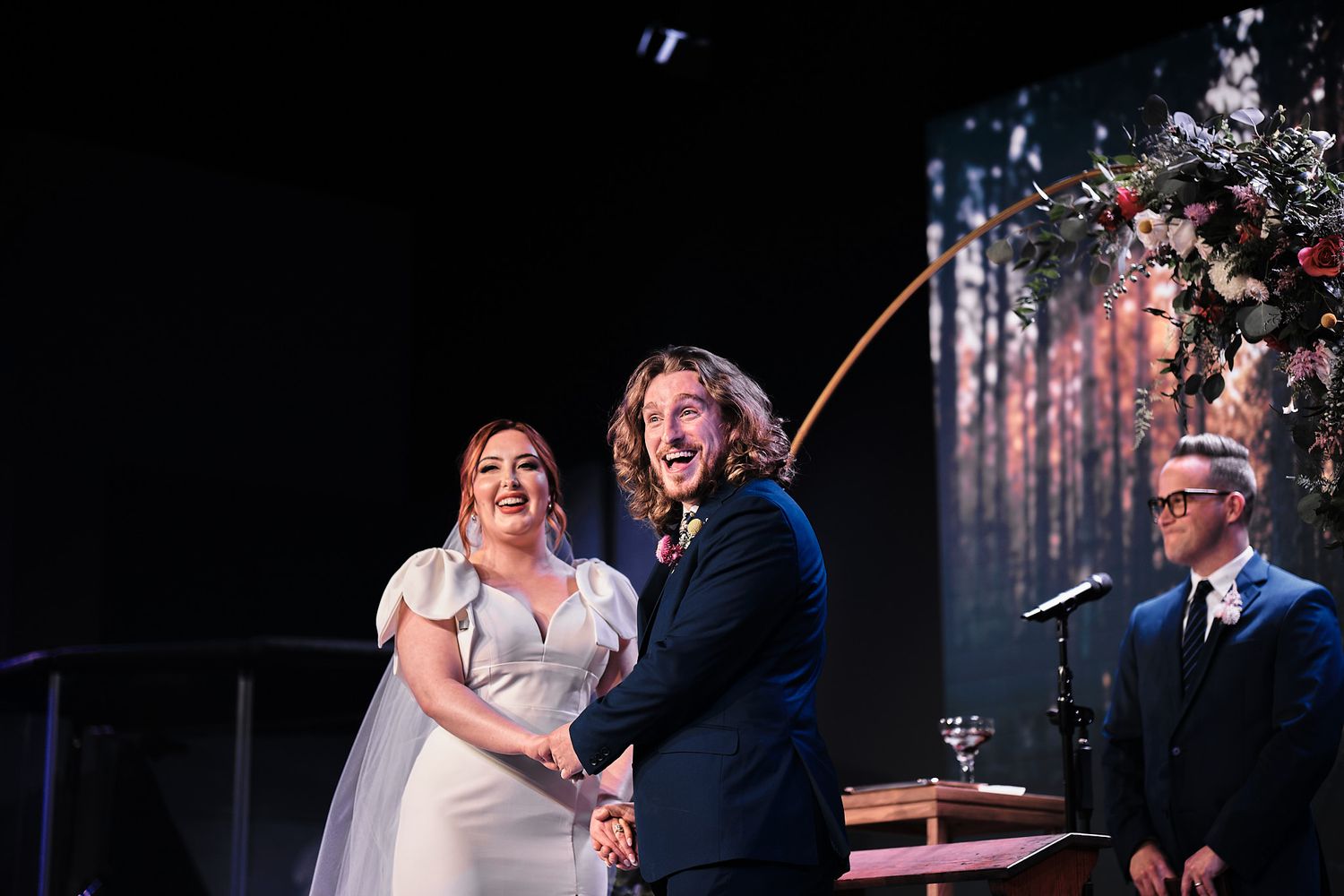 A wedding ceremony takes place on stage with celebrant and couple sharing a joyful moment.