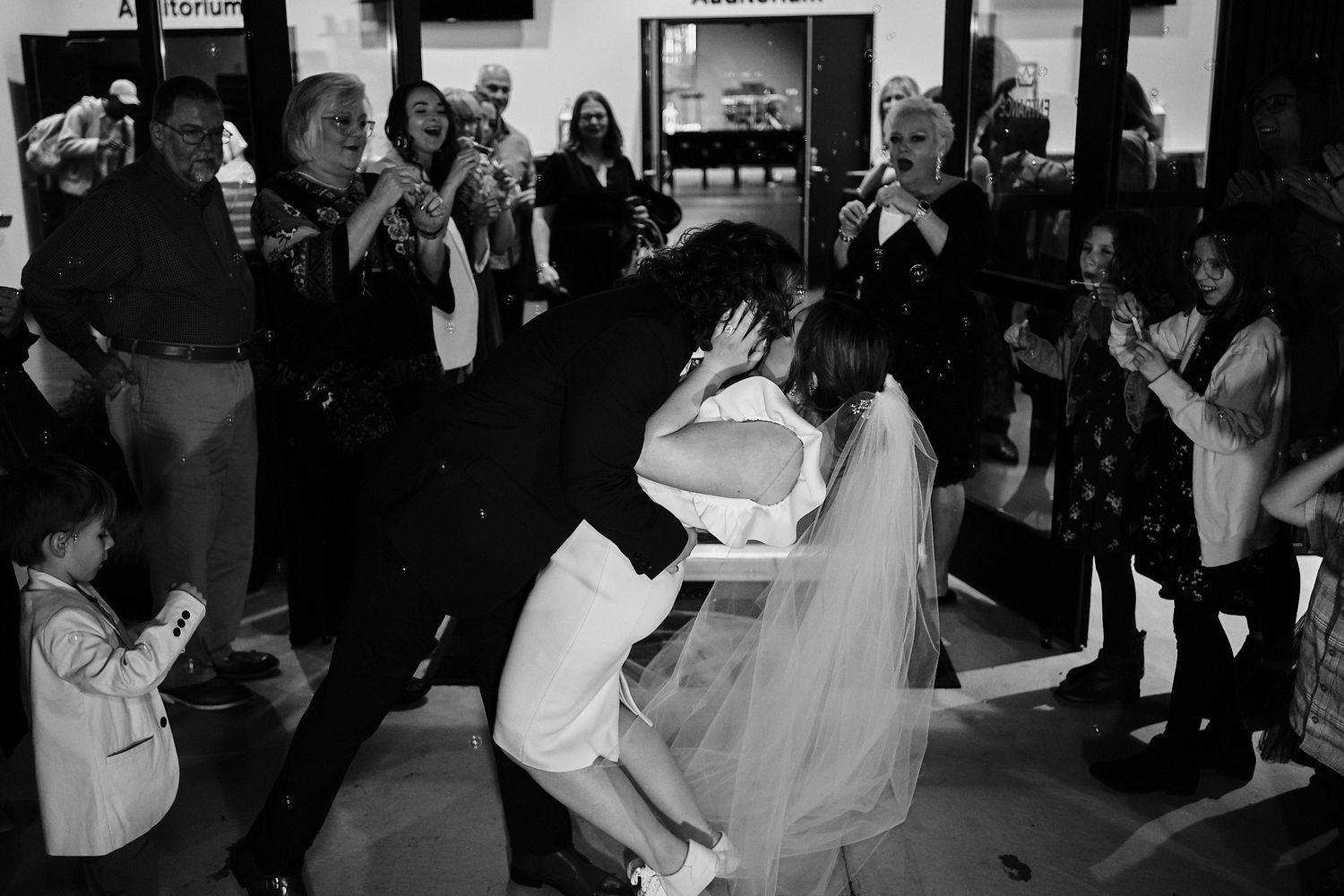 Wedding guests dance and celebrate at a reception captured in black and white photography.