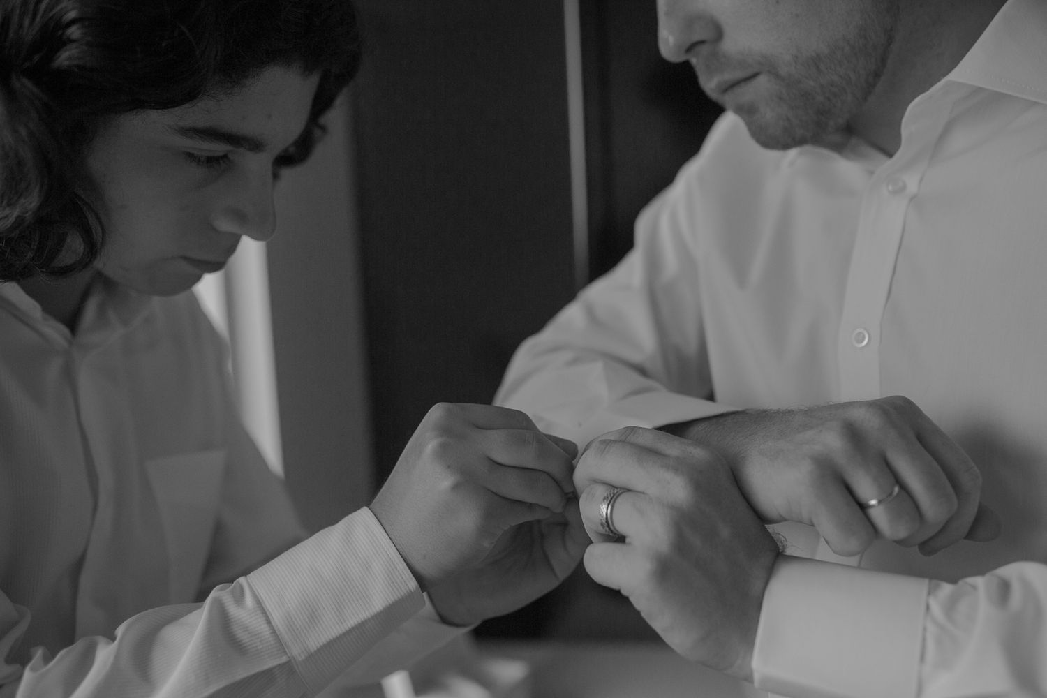 Black and white image showing two people examining wedding bands or rings up close.