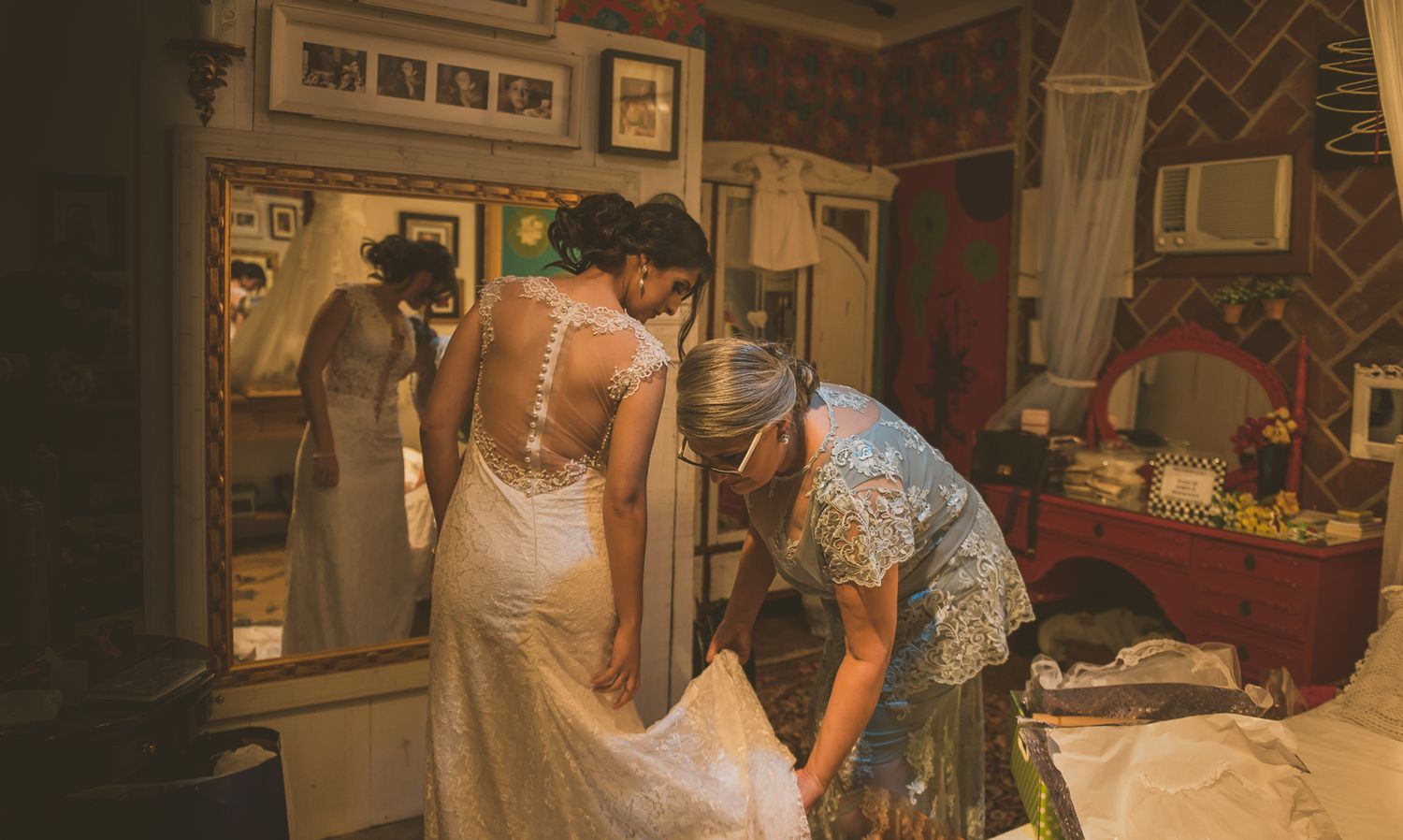 Wedding dress being adjusted in a room with vintage decor and mirrors.