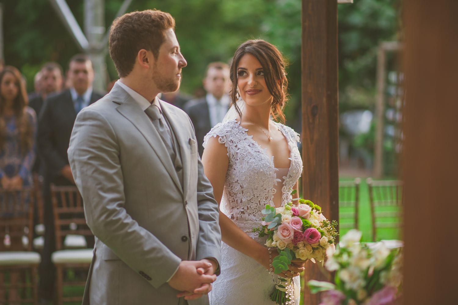 Couple in wedding attire standing together during outdoor ceremony.
