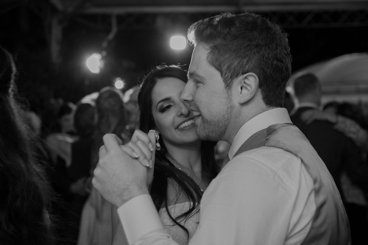 A couple shares an intimate slow dance under dim lighting at an evening reception celebration.