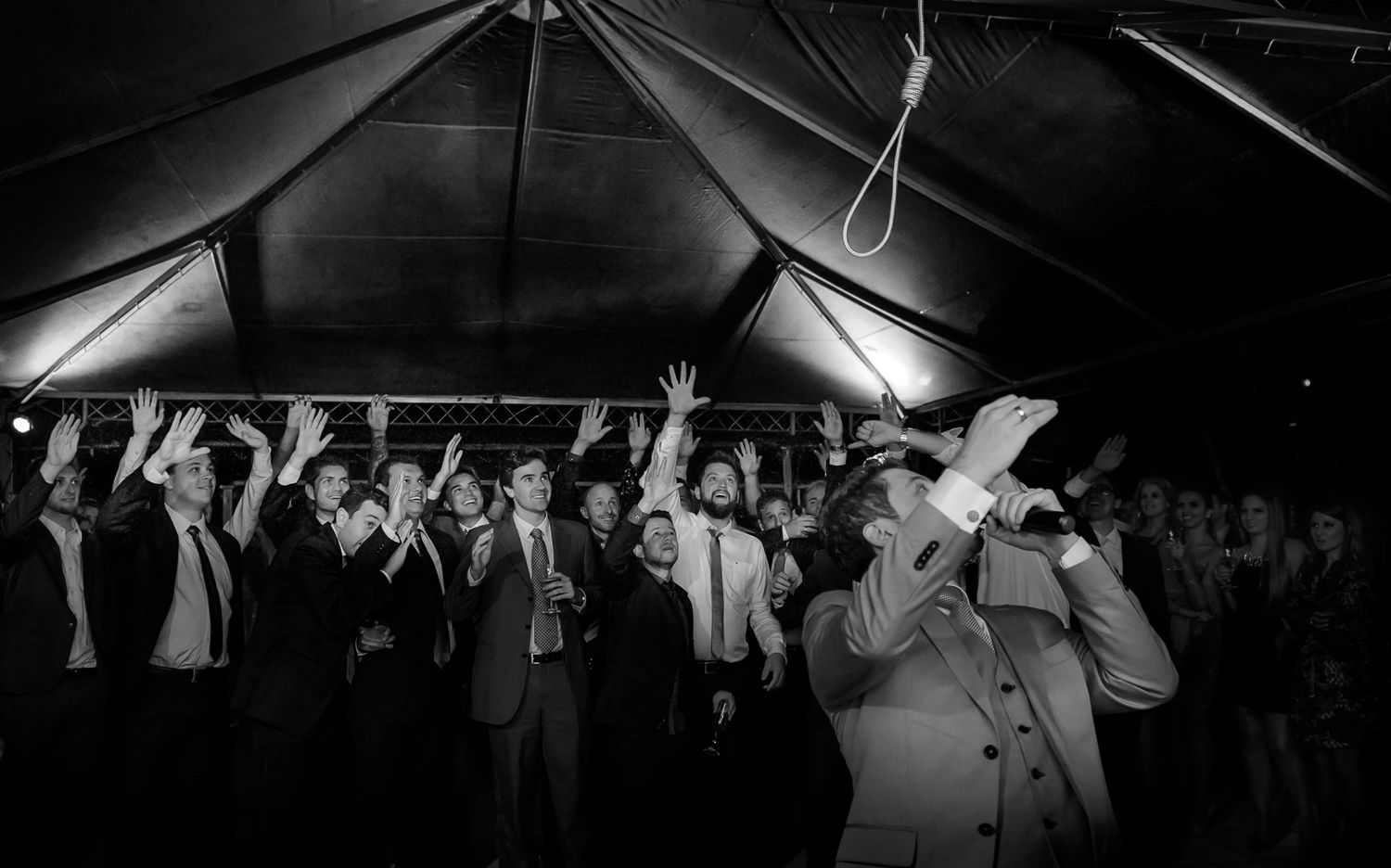 Party guests dancing and celebrating under a large tent at night.