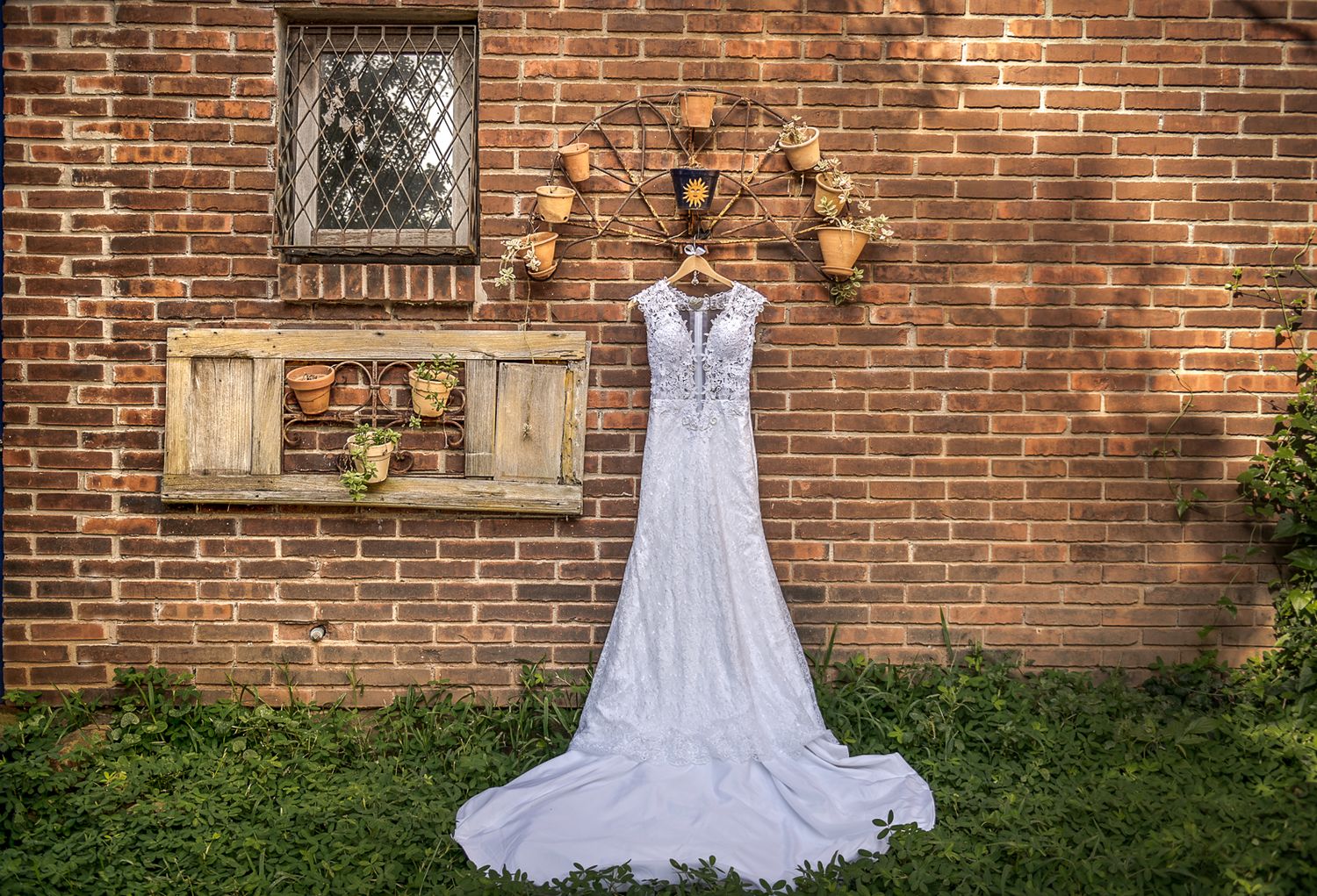 White lace wedding dress displayed against rustic brick wall with vintage decorative elements.