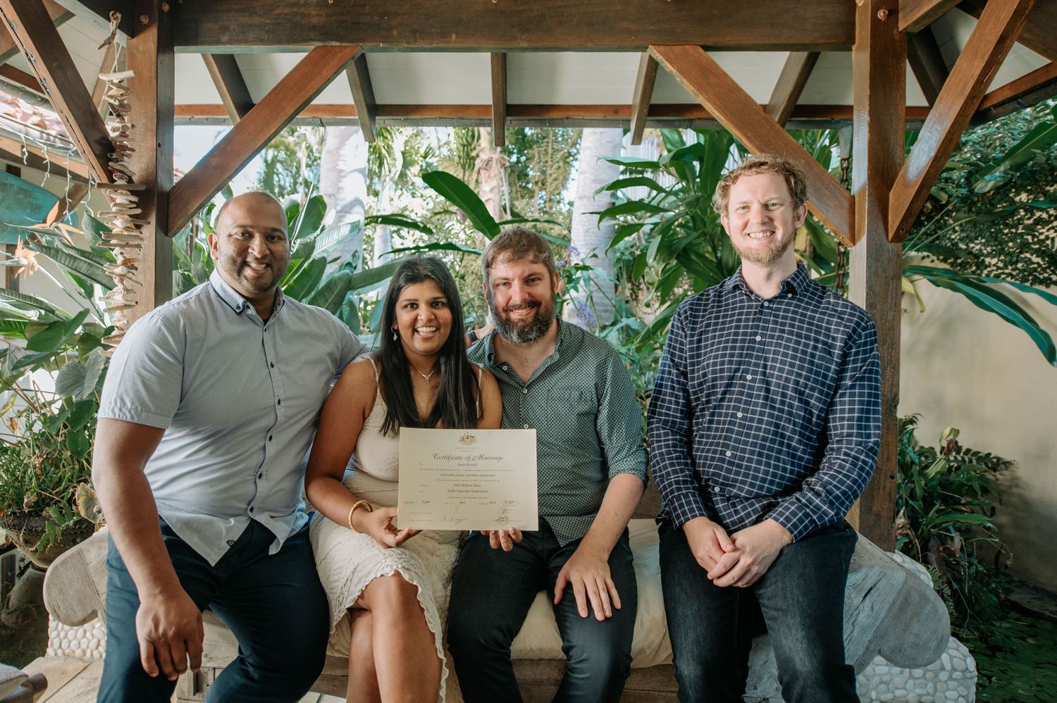 Four people sit together holding a document under a covered outdoor patio.