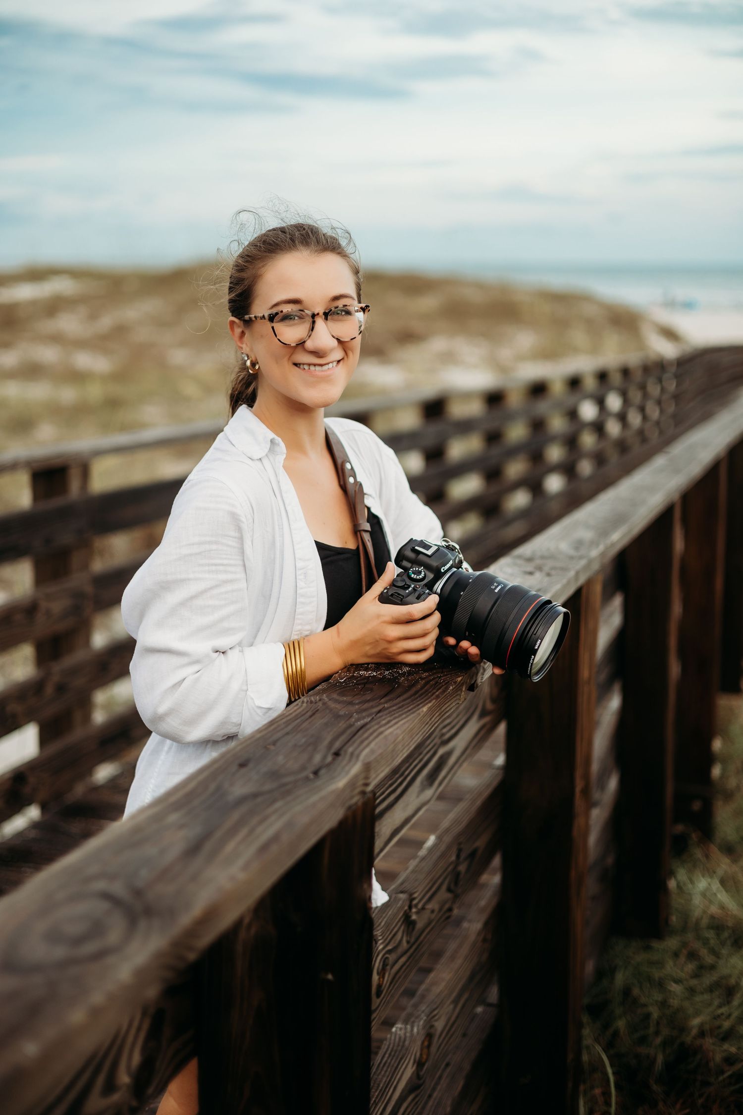 Photographer with camera on wooden boardwalk overlooking coastal landscape.