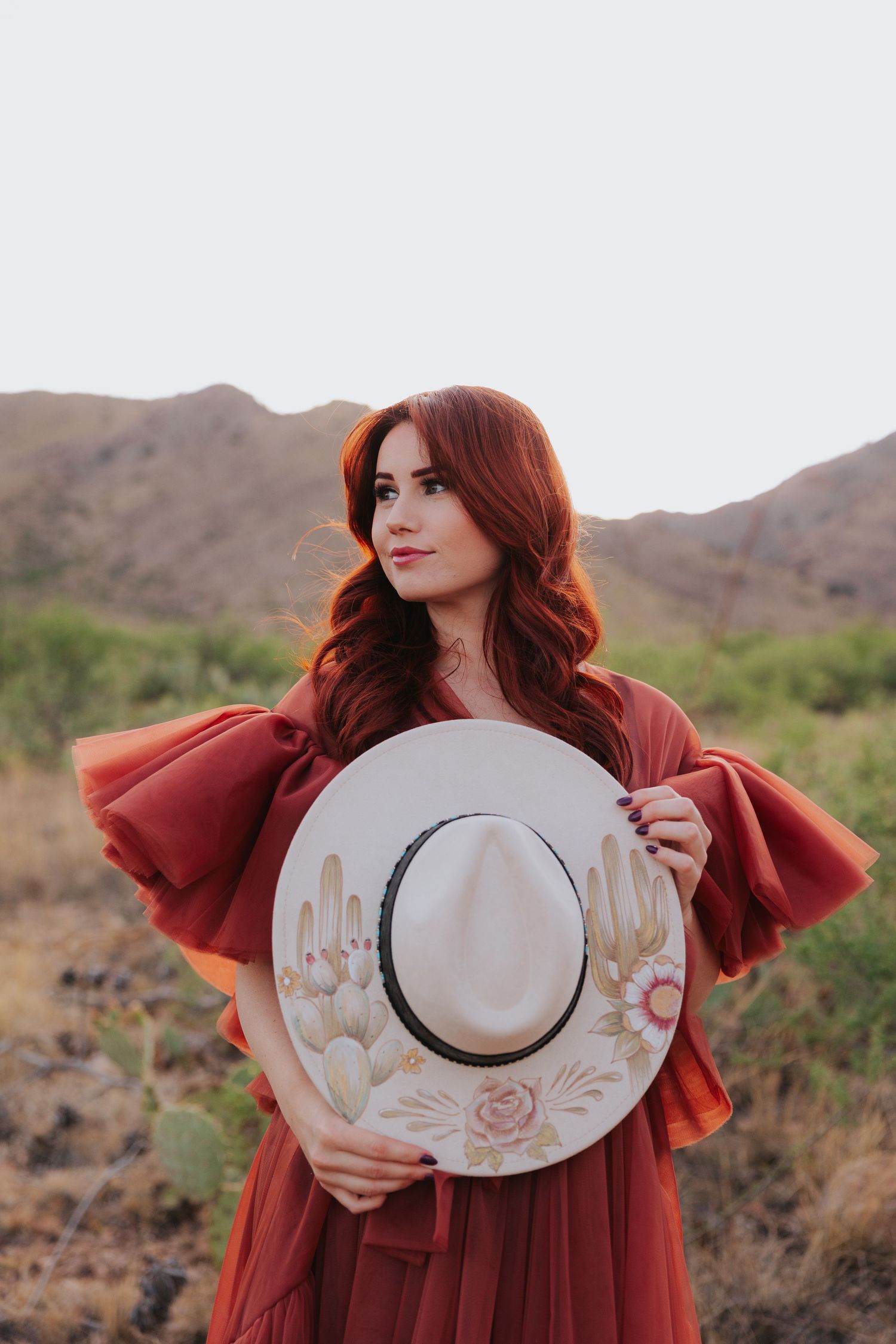 Desert fashion portrait with decorated wide-brimmed hat and red ruffled dress.
