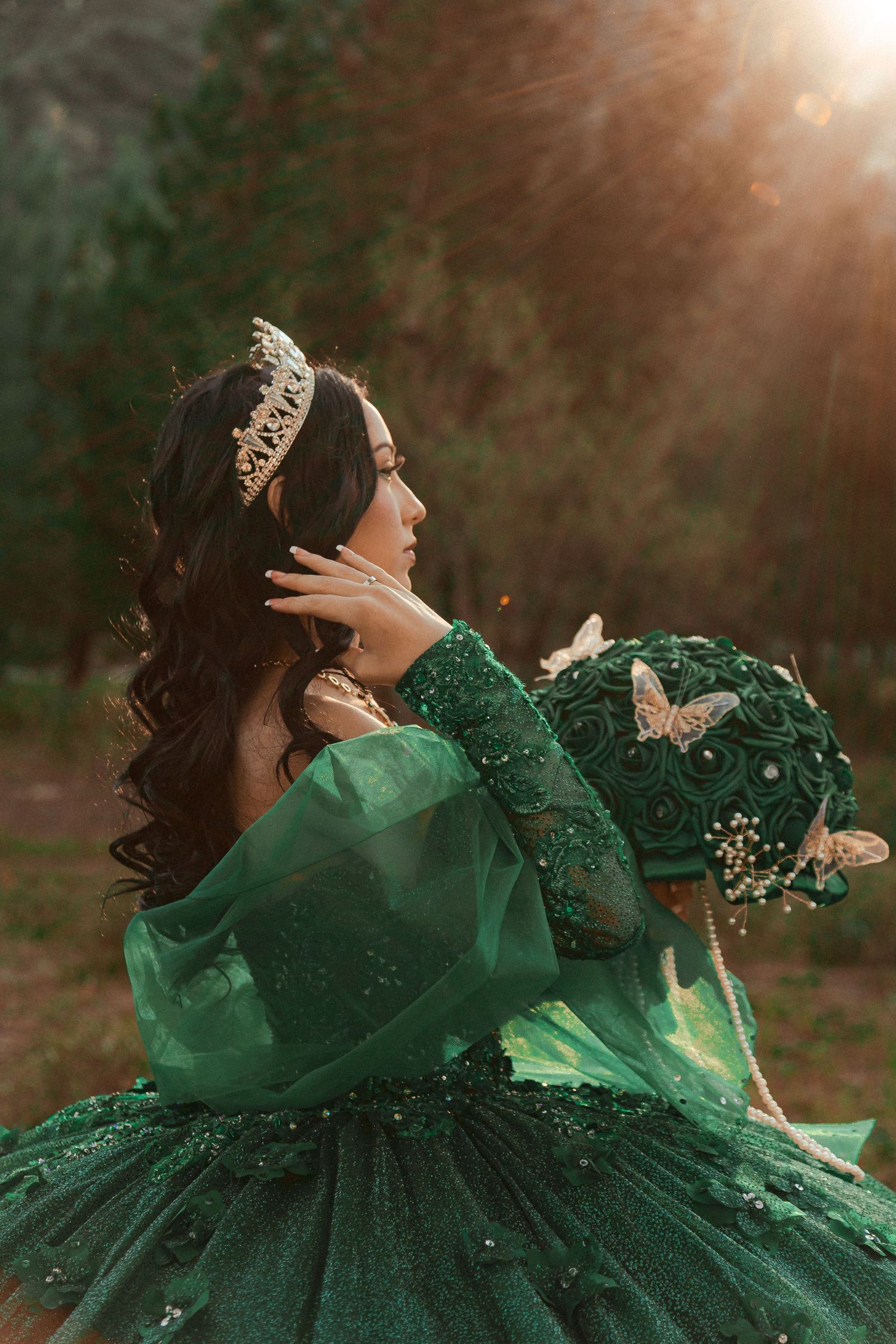 An emerald green ball gown adorned with butterflies captured in dramatic backlit forest lighting.