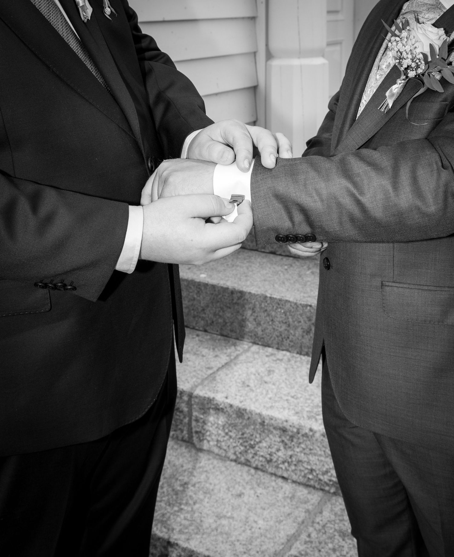 Two grooms in suits exchange wedding rings on church steps in classic black and white photo.