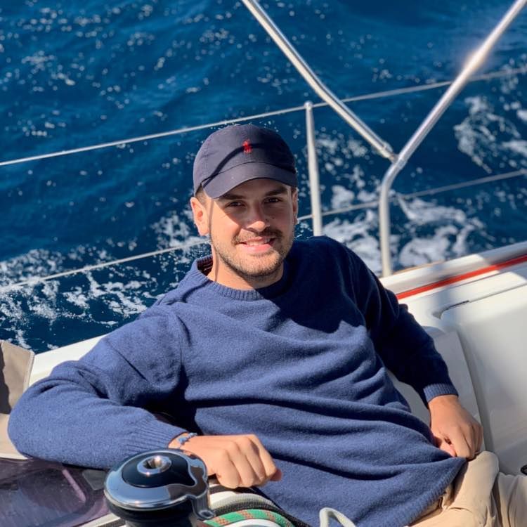 Person relaxing on a sailboat deck wearing blue sweater against ocean background.
