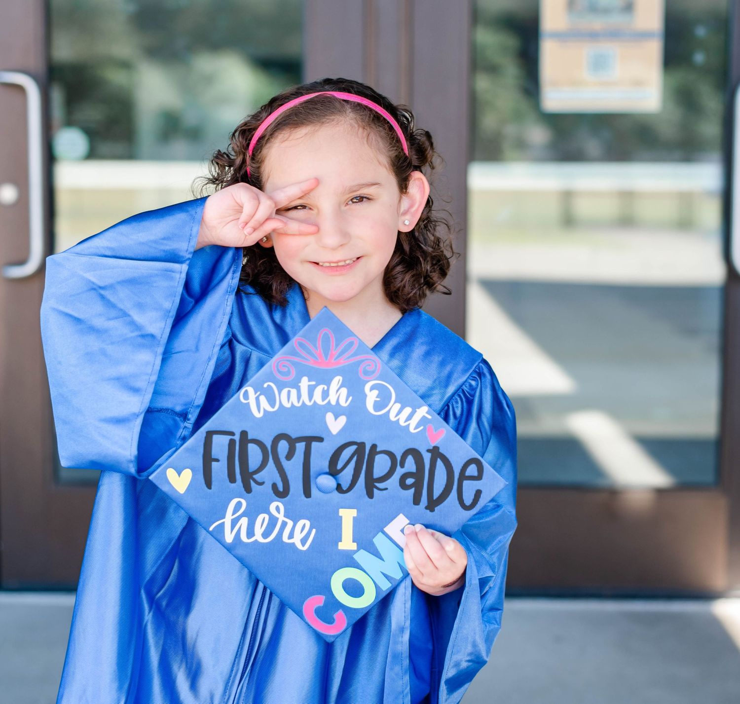 Student wearing bright blue graduation gown with "First Grade Here I Come" text displays excitement.