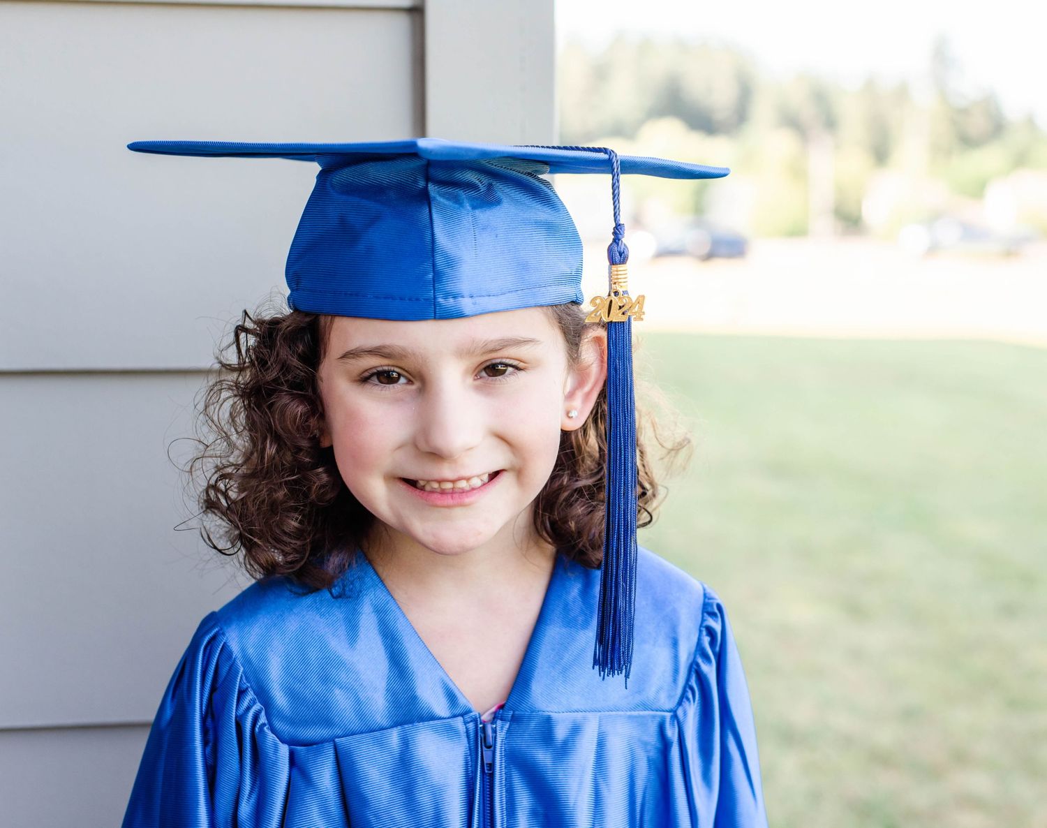 Graduate wearing blue cap and gown smiles while standing outside.