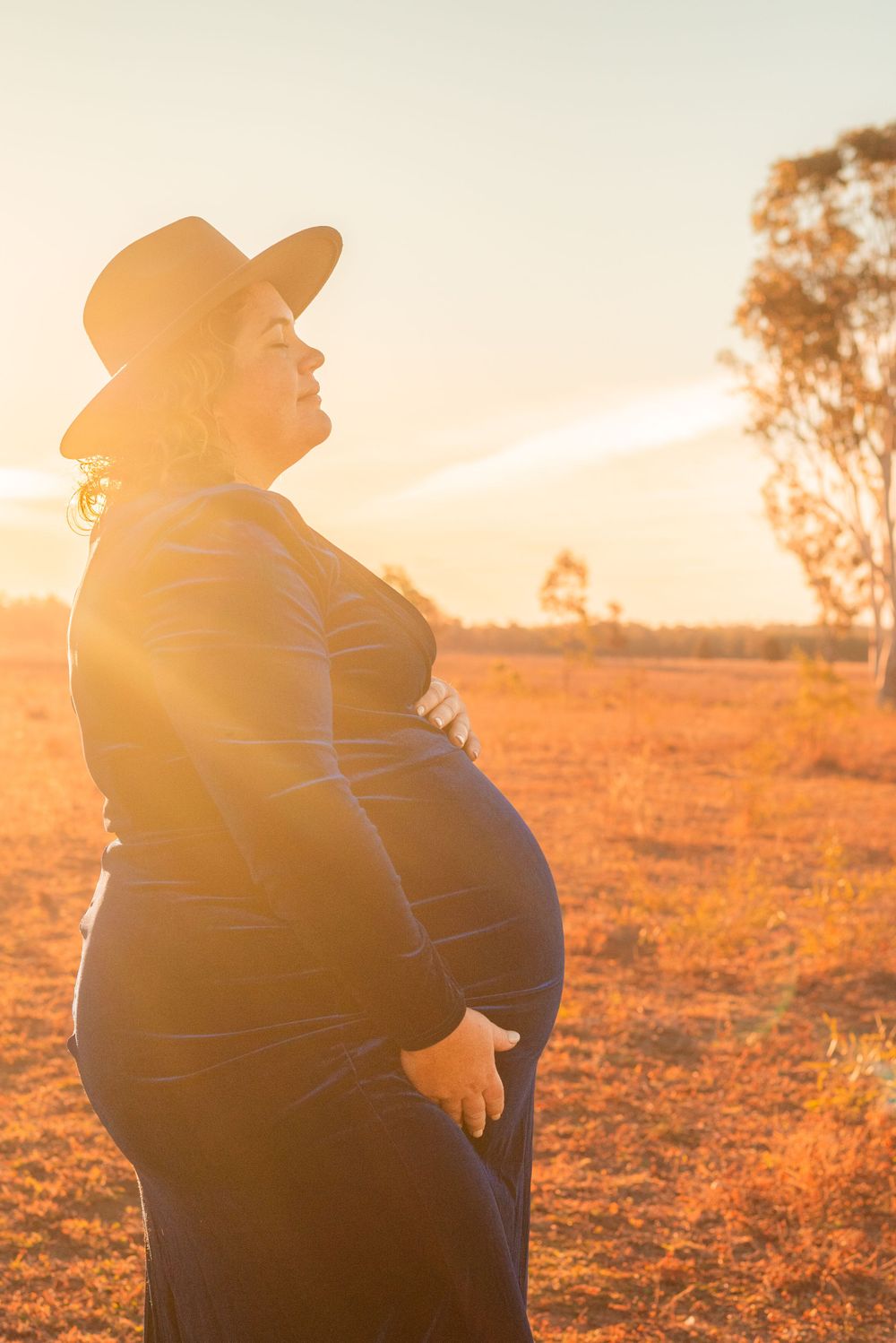 Side profile of expectant parent in cowboy hat during golden hour.