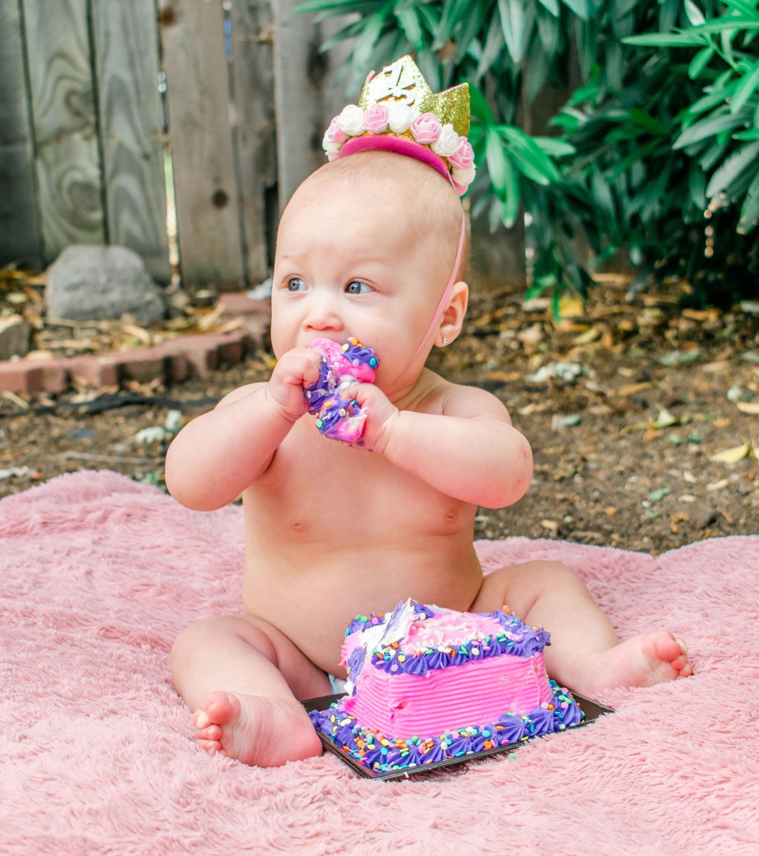 Outdoor cake smash photography session with crowned baby on pink blanket.