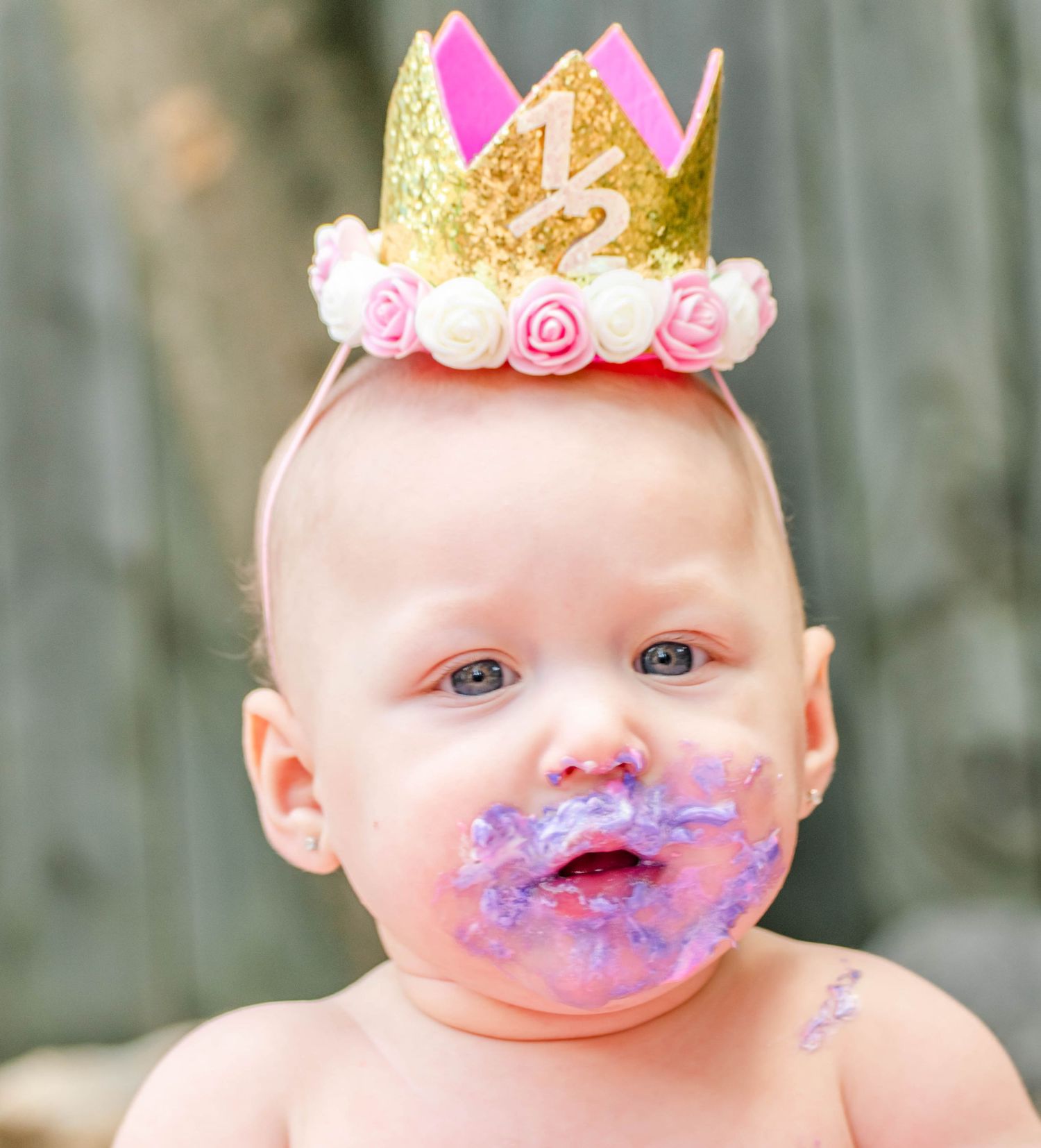 Baby wearing a pink and gold crown enjoys a messy purple cake smash photoshoot on pink backdrop.