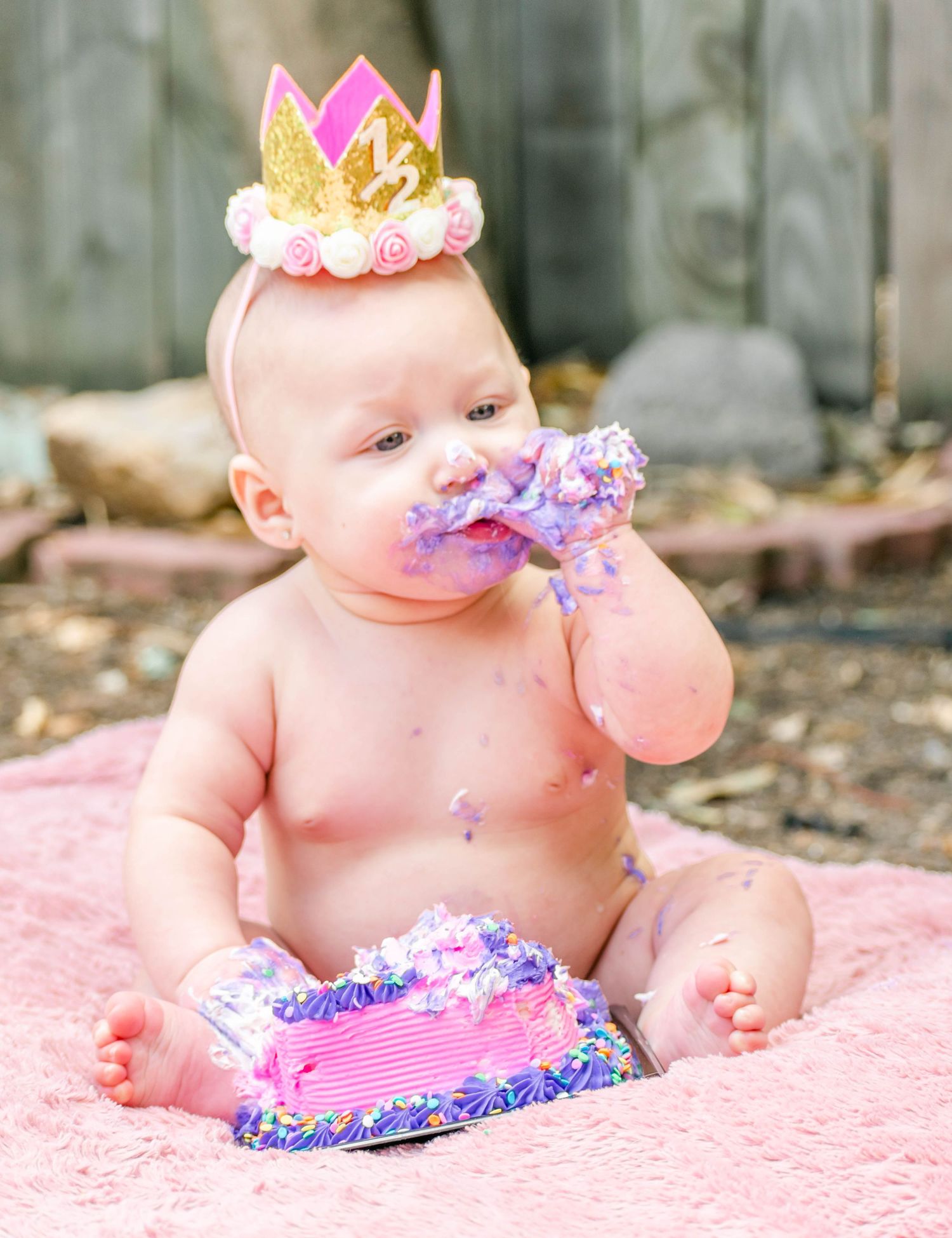First birthday cake smash session with baby wearing crown getting messy with purple frosting.