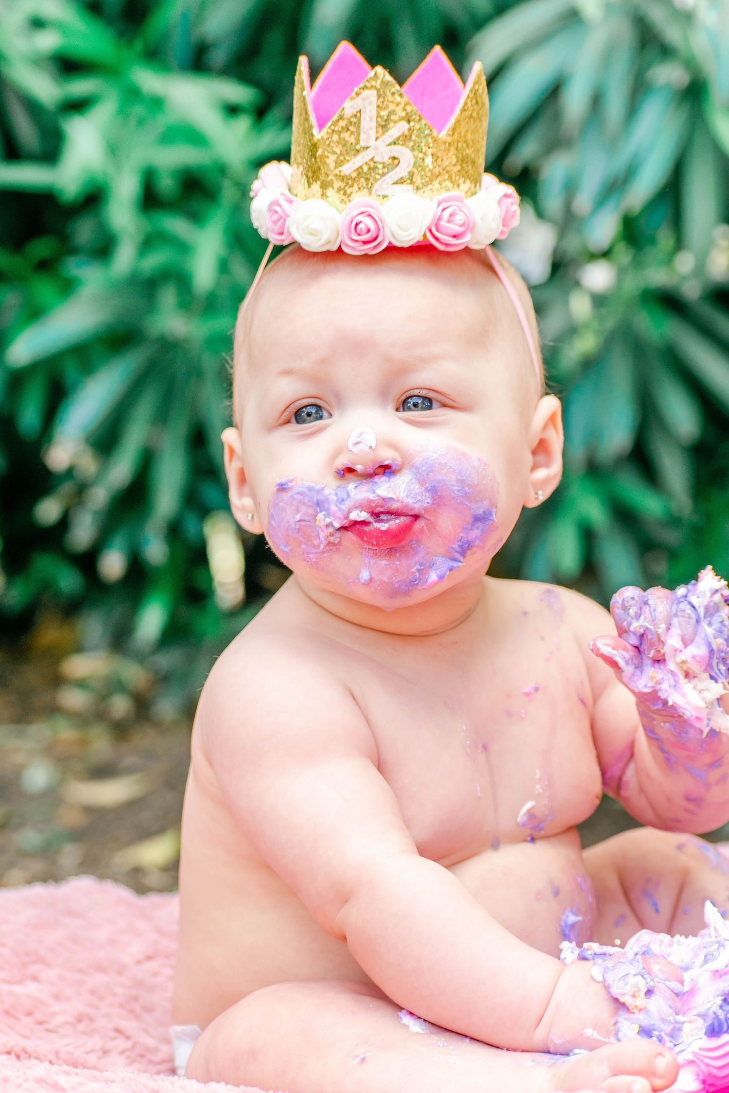 Cake smash photo series shows baby with crown getting messy with purple birthday cake.