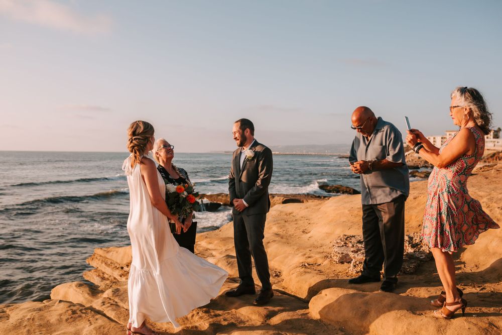 A small intimate wedding ceremony takes place on rocky cliffs overlooking the ocean at sunset.