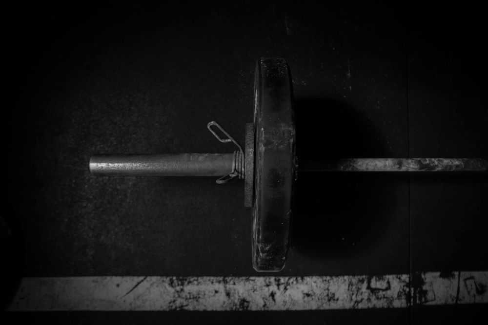 Close-up black and white shot of a weight plate on a barbell in dark lighting.