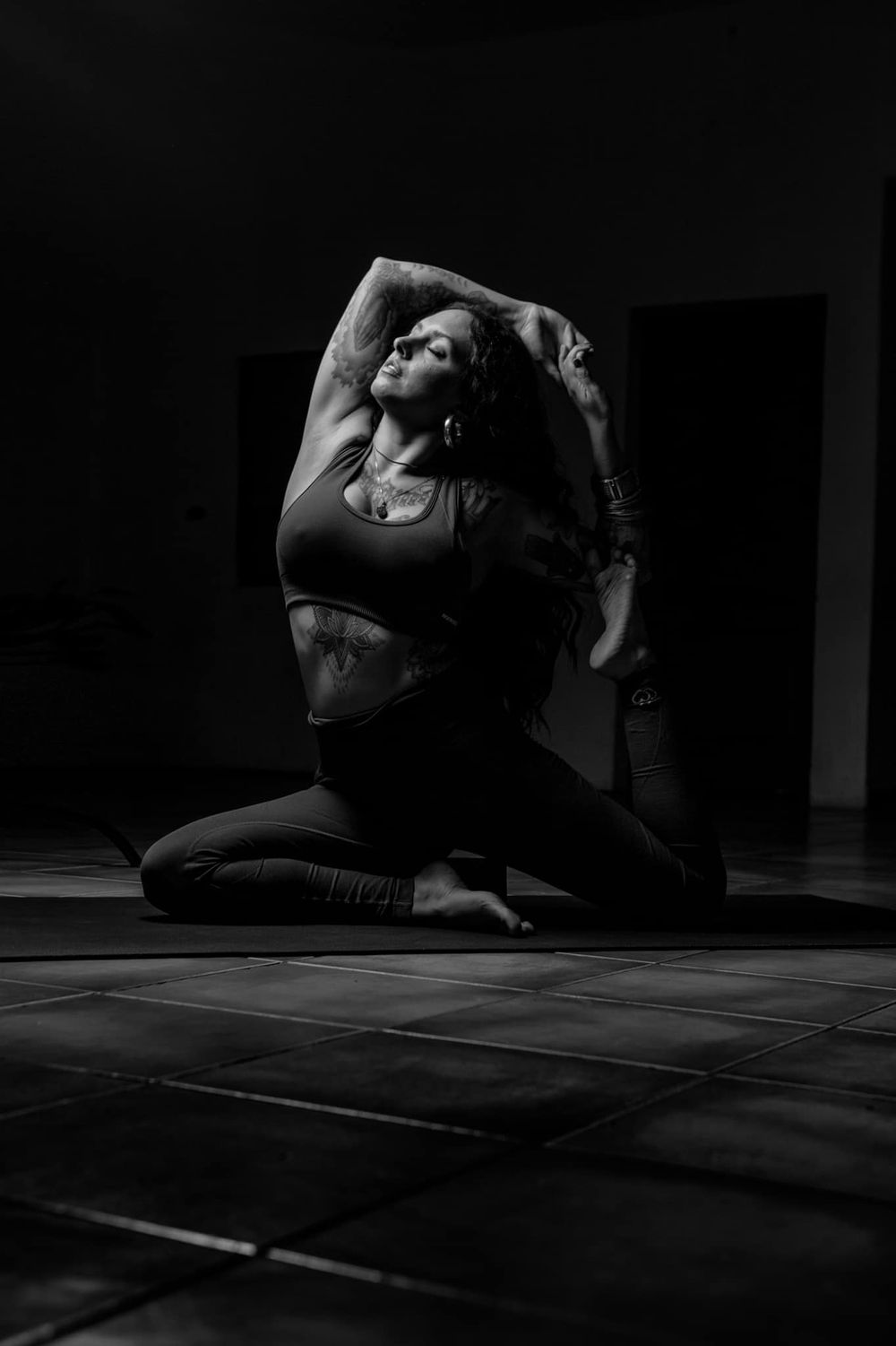 Dramatic black and white photo of a dancer in a flexible pose on a tiled floor.