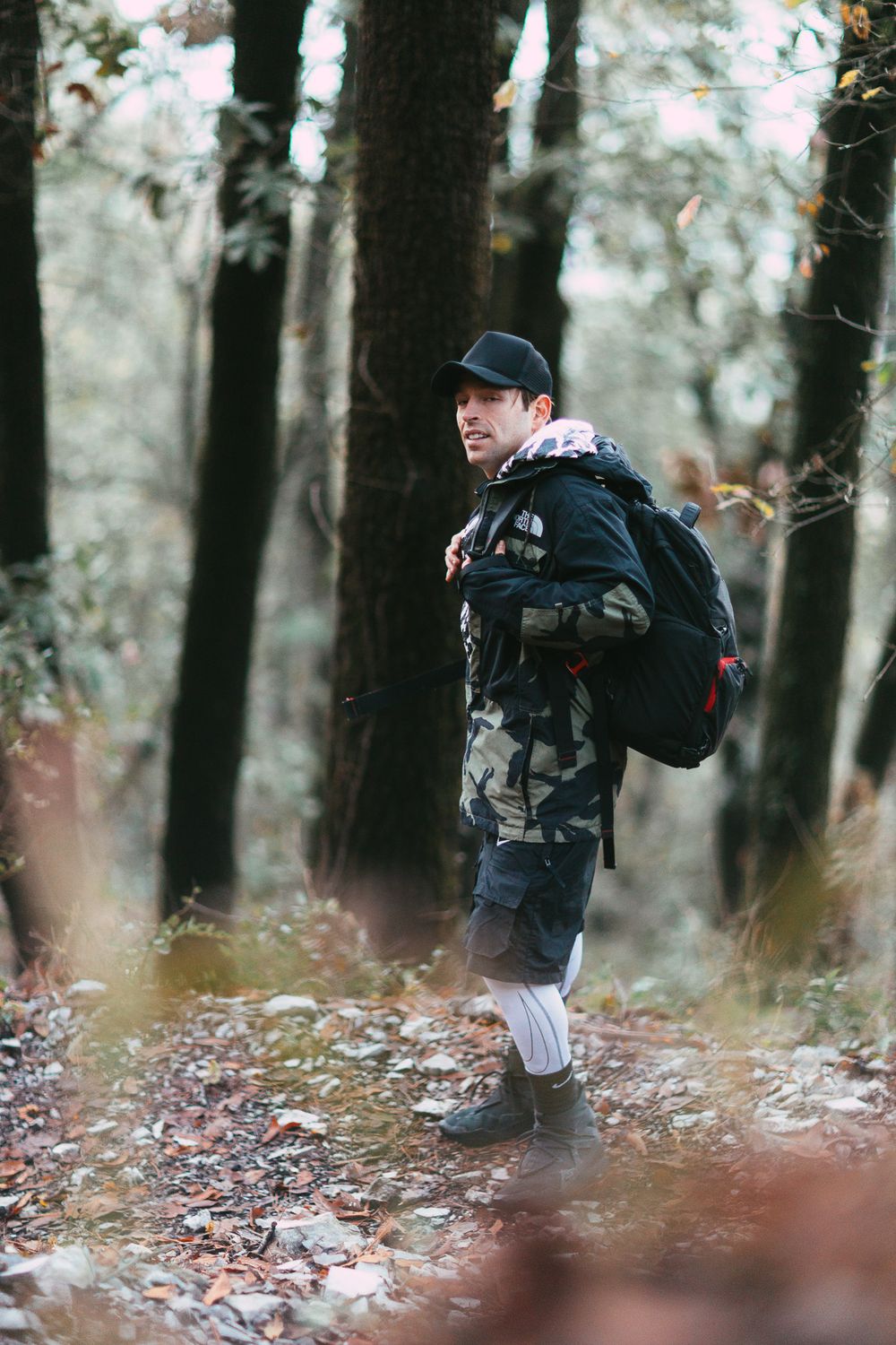 Hiker in winter gear and backpack walks through misty forest trail with fallen leaves.